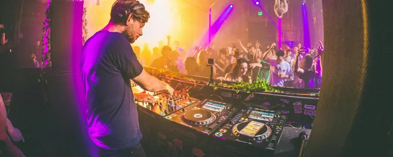 Elektronisk artist spelar live som DJ bakom mixerbord inför publik med färgstarka scenljus