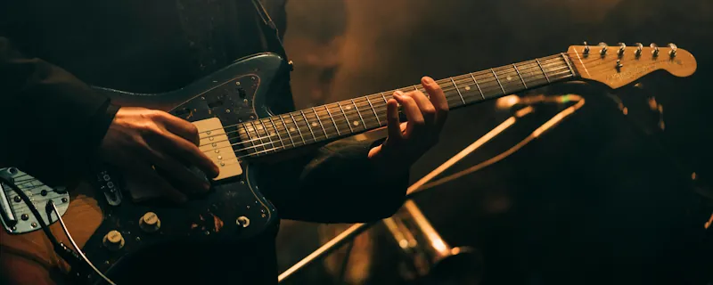 Bluesgitarrist spelar elgitarr under varmt scenljus i mörk miljö