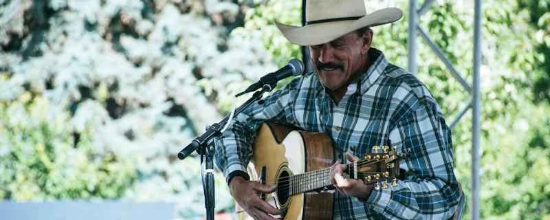 Countryartist spelar akustisk gitarr och sjunger live med cowboyhatt på scen utomhus