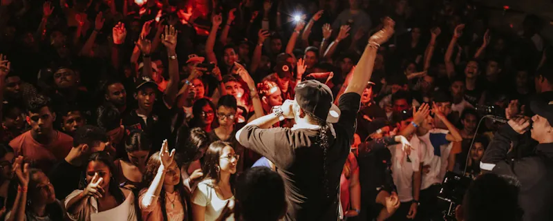 Hiphopartist uppträder live med mikrofon inför publik på konsert med röd scenbelysning