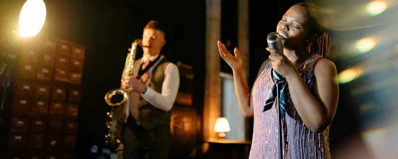 Jazzsångerska uppträder med mikrofon medan saxofonist spelar i bakgrunden under liveframträdande