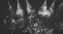 Rockband uppträder live på scen inför publik under konsert med klassisk rockscenografi och scenljus.