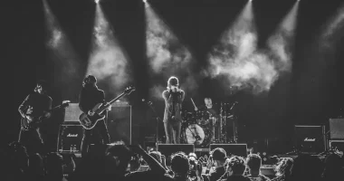 Rockband uppträder live på scen inför publik under konsert med klassisk rockscenografi och scenljus.