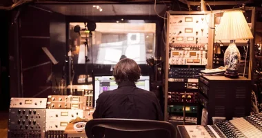Person sitter i en musikstudio framför mixerbord och ljudutrustning, symbol för svensk musikproduktion och svenska artister som format musikhistorien.